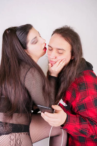 Mulher sexy atraente está seduzindo o homem nerd enquanto ele usa o smartphone no fundo branco — Fotografia de Stock