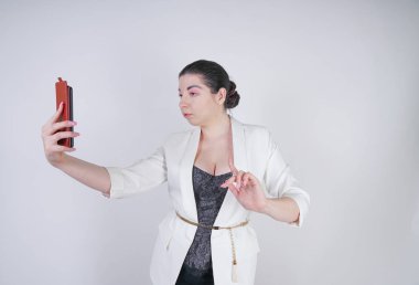 büyüleyici mix yarış artı beyaz bir iş ceketi boyutu kadın Studio beyaz arka planda elinde akıllı telefon ile selfie fotoğraf çekmek