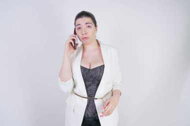 büyüleyici mix yarış artı beyaz bir iş ceketi studio beyaz arka plan üzerinde elinde akıllı telefon ile mutsuz ve üzgün ayakta boyutu kadın