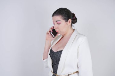 büyüleyici mix yarış artı beyaz bir iş ceketi studio beyaz arka plan üzerinde elinde akıllı telefon ile mutsuz ve üzgün ayakta boyutu kadın