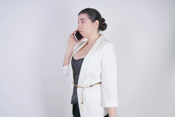 Kouzelný mixový závod plus velikostní žena v bílém podnikatelovém kabátku, který je nešťastný a smutný s chytrou telefonem v ruce na bílém pozadí ve studiu — Stock fotografie