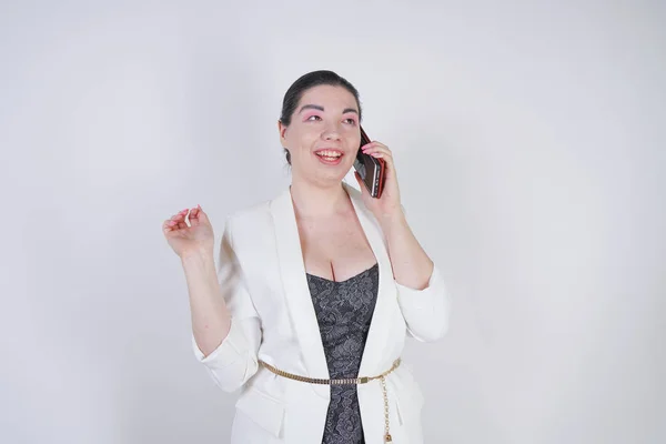 Ευτυχισμένο Mix αγώνα συν το μέγεθος γυναίκα σε ένα λευκό επιχειρηματικό μπουφάν καλώντας και μιλώντας με το smartphone στο χέρι σε λευκό φόντο στο στούντιο — Φωτογραφία Αρχείου