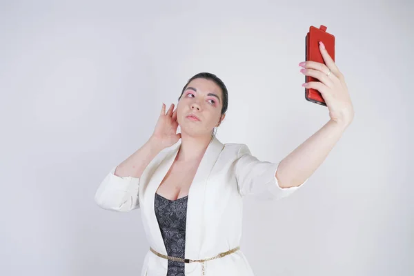 Charmante mix race plus size vrouw in een witte Business jas staande met slimme telefoon in de hand op witte achtergrond in Studio — Stockfoto