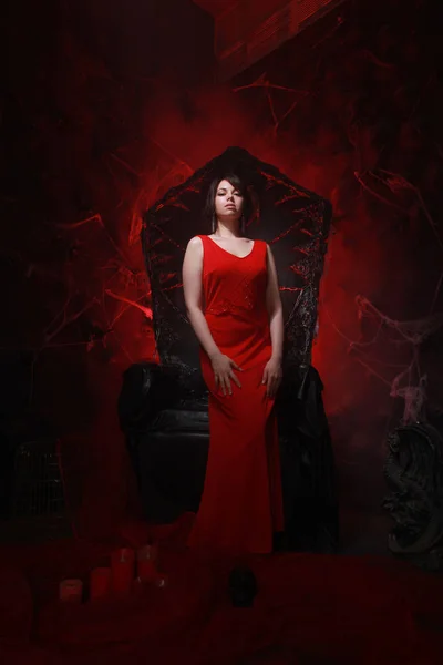 Beautiful lonely girl in long red dress on the halloween throne ready for scary party — Stock Photo, Image