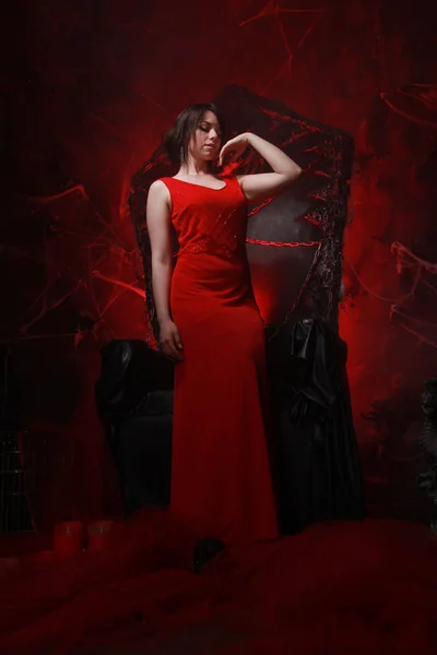 Hermosa chica solitaria en vestido largo rojo en el trono de Halloween listo para la fiesta de miedo — Foto de Stock