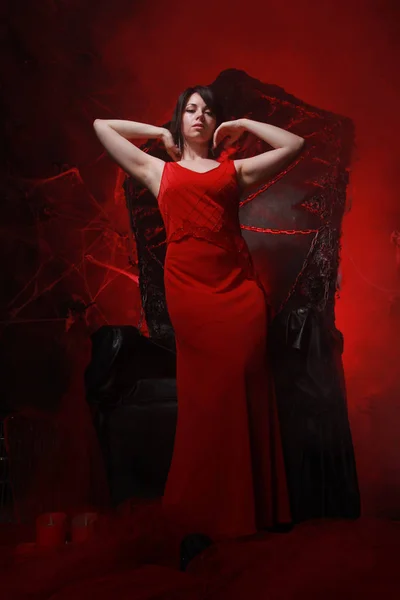 Hermosa chica solitaria en vestido largo rojo en el trono de Halloween listo para la fiesta de miedo —  Fotos de Stock