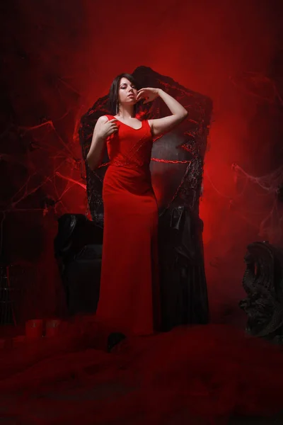 Hermosa chica solitaria en vestido largo rojo en el trono de Halloween listo para la fiesta de miedo — Foto de Stock