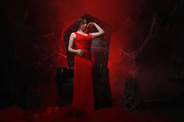 Bela menina solitária em vestido vermelho longo no trono halloween pronto para festa assustadora — Fotografia de Stock