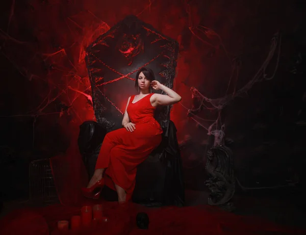 Schöne einsame Mädchen in langen roten Kleid auf dem Halloween-Thron bereit für gruselige Party — Stockfoto