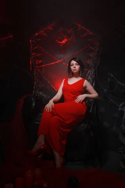 Hermosa chica solitaria en vestido largo rojo en el trono de Halloween listo para la fiesta de miedo — Foto de Stock