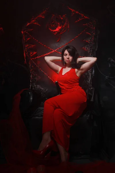 Hermosa chica solitaria en vestido largo rojo en el trono de Halloween listo para la fiesta de miedo —  Fotos de Stock