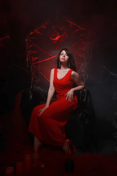 Красивая одинокая девушка в длинном красном платье на Хэллоуинском троне готова к страшной вечеринке — стоковое фото