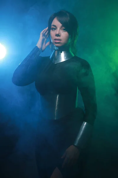 Modelo de moda futurista con ropa negra y plateada y de pie en el colorido humo azul y verde — Foto de Stock