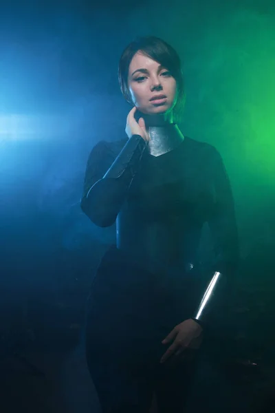 Modelo de moda futurista con ropa negra y plateada y de pie en el colorido humo azul y verde —  Fotos de Stock