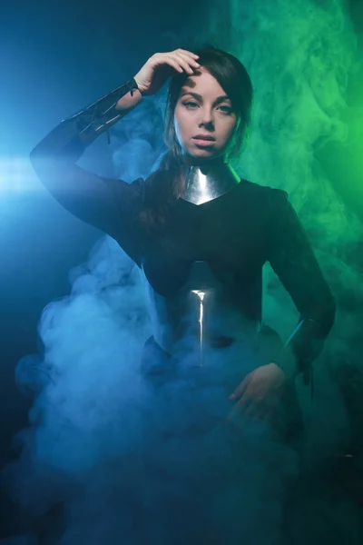 Modelo de moda futurista con ropa negra y plateada y de pie en el colorido humo azul y verde — Foto de Stock