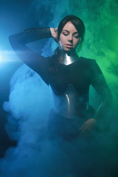 Modelo de moda futurista con ropa negra y plateada y de pie en el colorido humo azul y verde —  Fotos de Stock