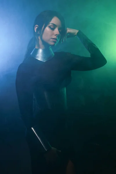 Futuristisk mode modell klädd i svart och silver kläder och stående i färgglada blå och grön rök — Stockfoto