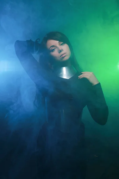 Modelo de moda futurista con ropa negra y plateada y de pie en el colorido humo azul y verde —  Fotos de Stock