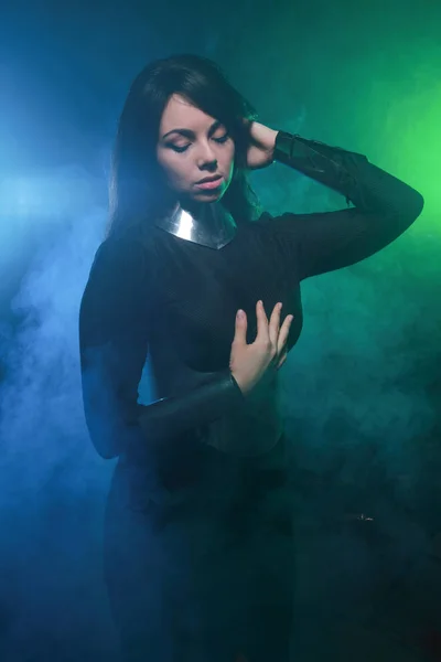 Футуристическая модель в черно-серебристой одежде, стоящая в ярком синем и зеленом дыму — стоковое фото