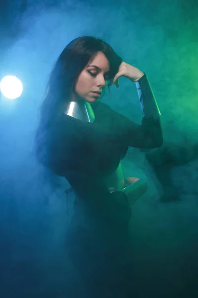 Modelo de moda futurista con ropa negra y plateada y de pie en el colorido humo azul y verde — Foto de Stock