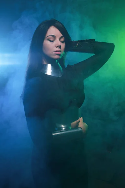 Modelo de moda futurista con ropa negra y plateada y de pie en el colorido humo azul y verde —  Fotos de Stock