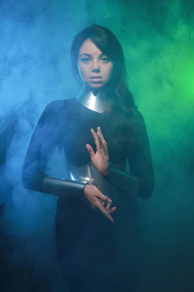 Modelo de moda futurista con ropa negra y plateada y de pie en el colorido humo azul y verde — Foto de Stock