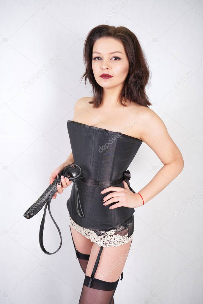Sensual woman in black costume with leather whip on white studio background