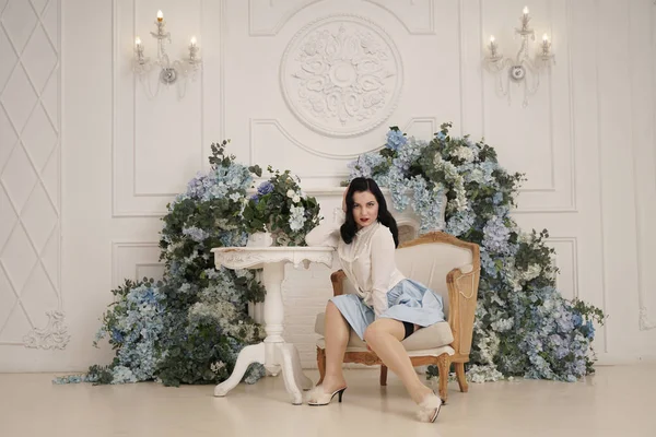 Pin up menina em um apartamento branco retro perto da mesa. Mulher vintage bonita em quarto elegante com flores sozinho . — Fotografia de Stock