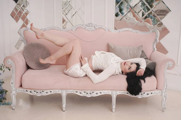 Preciosa mujer morena en pijama blanco lindo resto con sofá rosa solo en apartamento blanco solo — Foto de Stock
