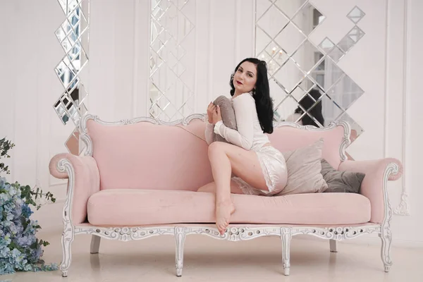 Прекрасна брюнетка в білій милій піжамі відпочиває з рожевим диваном наодинці в білій квартирі — стокове фото