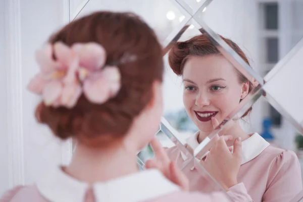 Menina em vestido vintage em olhar no espelho alegre e feliz. bonito jovem mulher no rosa retro vestido sozinho no branco quarto . — Fotografia de Stock