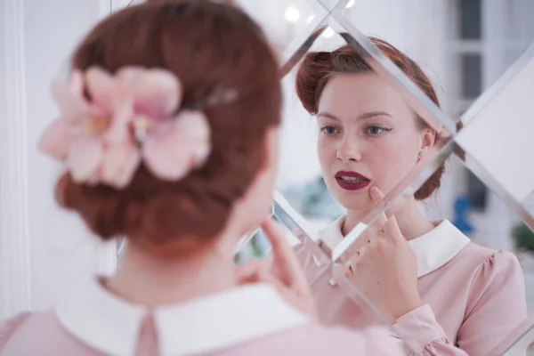 Girl in vintage dress in looking in mirror cheerful and happy. Cute young woman in pink retro dress alone in white room. — Stock Photo, Image