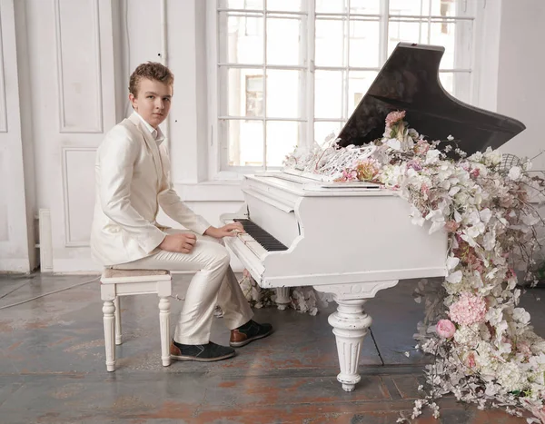 Ung man Tonåring i en vit affärs dräkt med ett stort vitt piano i blommor. kaukasiska manliga spela musik på semester ensam. — Stockfoto