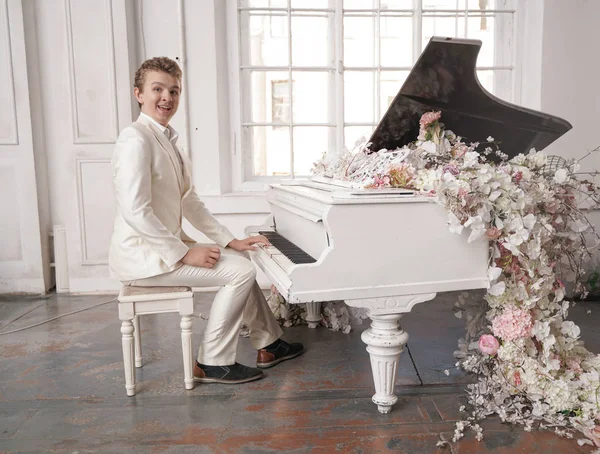 Ung man Tonåring i en vit affärs dräkt med ett stort vitt piano i blommor. kaukasiska manliga spela musik på semester ensam. — Stockfoto