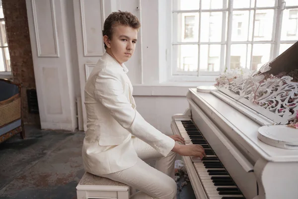 Ung man Tonåring i en vit affärs dräkt med ett stort vitt piano i blommor. kaukasiska manliga spela musik på semester ensam. — Stockfoto
