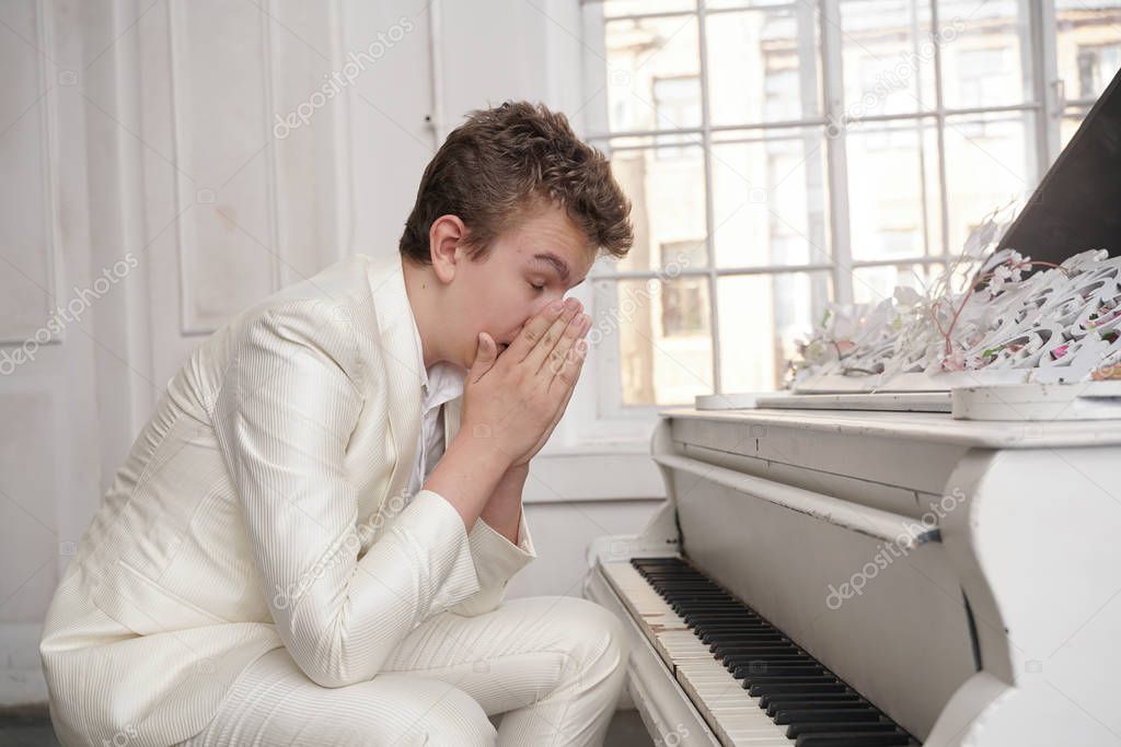 young teenager man in depression with white big grand piano indoors alone. guy hates music and nervous