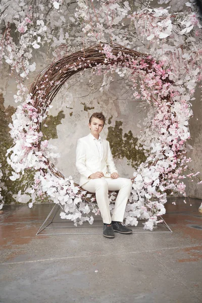 Encantador guapo joven caucásico en un traje de negocios blanco, chaqueta y pantalones, posando contra un Sakura rosa . — Foto de Stock