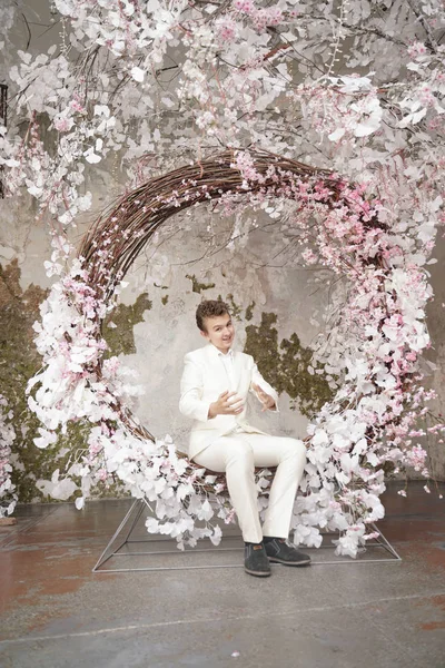 Encantador guapo joven caucásico en un traje de negocios blanco, chaqueta y pantalones, posando contra un Sakura rosa . — Foto de Stock