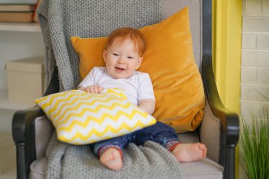 küçük çocuk bir sandalyede oturur ve elinde bir yastık tutar.