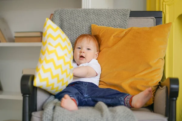 Klein kind zit in een stoel en houdt een kussen in zijn handen. — Stockfoto