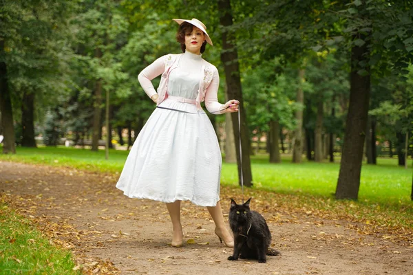 Hübsche alte Frau spaziert mit ihrer schwarzen Katze Maine Coon durch den Park — Stockfoto