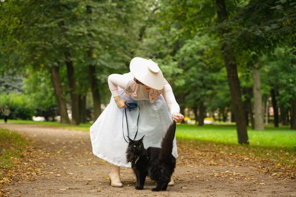 Bella donna vintage a piedi con il suo gatto nero maine bozzolo nel parco — Foto Stock