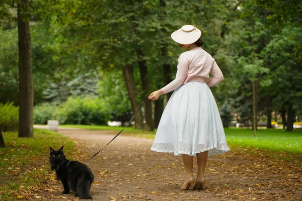 Красивая винтажная женщина, гуляющая со своим черным котом Мэном Куном в парке — стоковое фото