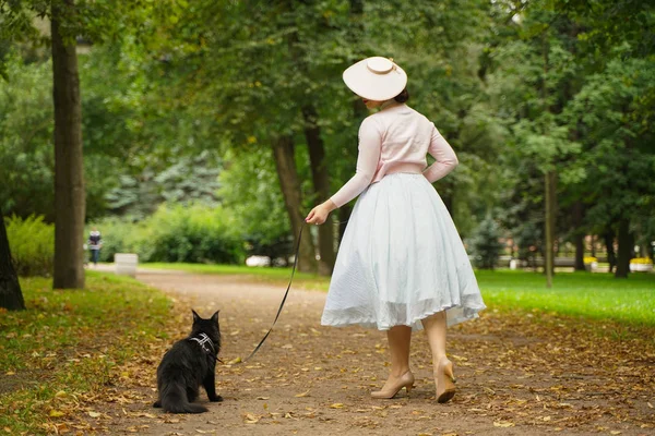 Mulher vintage bonita andando com seu casulo maine gato preto no parque — Fotografia de Stock