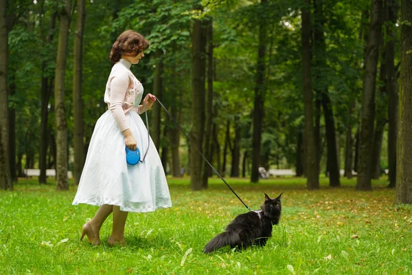 Pretty vintage woman walking with her black cat maine coon in the park — Stock Photo, Image