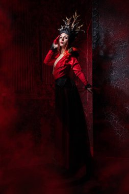 kırmızı duman ile büyük bir kapının arka planda uzun lüks bir elbise ağaç kökleri şeklinde boynuzları ile güzel moda cadı kadın. Cadılar Bayramı konsepti