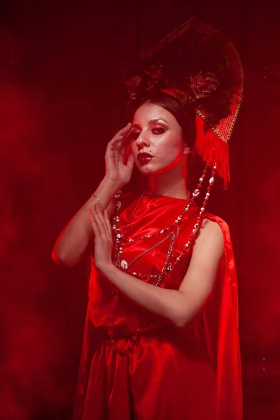 Rigorosa ragazza elegante in un abito rosso lungo alla moda e un cappello voluminoso sullo sfondo di fumo nello studio di notte da solo. Concetto Halloween . — Foto Stock