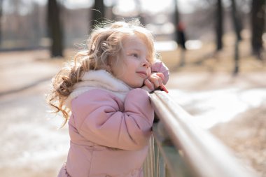 Pembe ceketli güzel kız tek başına soğuk bahar şehir parkında yürüyor