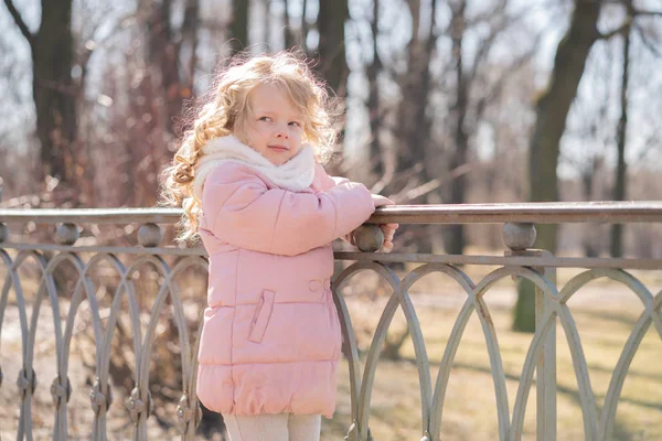 Mooi klein meisje in roze jas wandelen in het koude voorjaar City Park alleen — Stockfoto