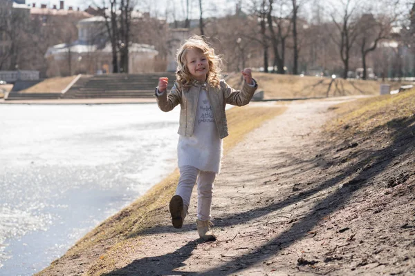 Criança feliz pulando e correndo no frio parque da cidade da primavera sozinho — Fotografia de Stock